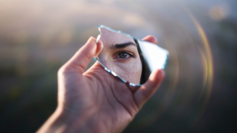 Close-up of hand holding a circular mirror with soft glow and bokeh background.